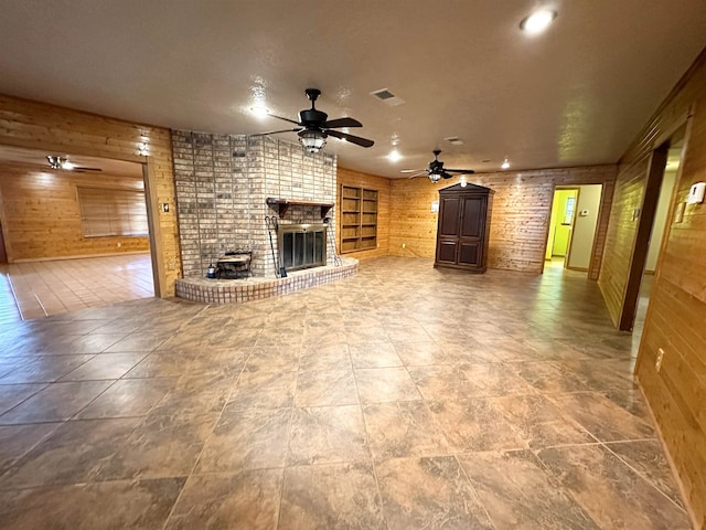 unfurnished living room featuring visible vents, ceiling fan, wooden walls, and a fireplace