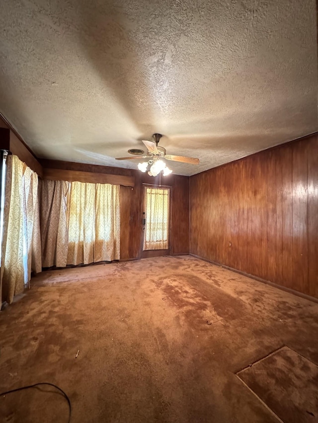 carpeted empty room with a textured ceiling, ceiling fan, and wooden walls