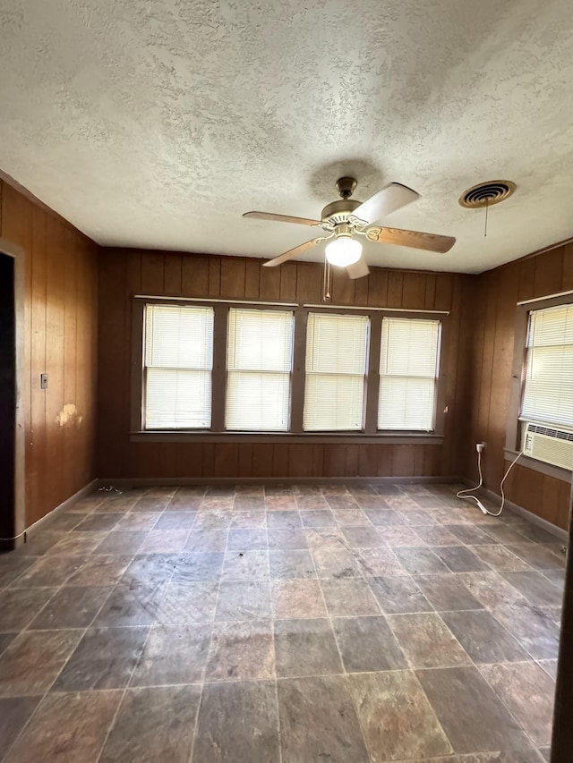 spare room featuring ceiling fan, cooling unit, a textured ceiling, and wooden walls