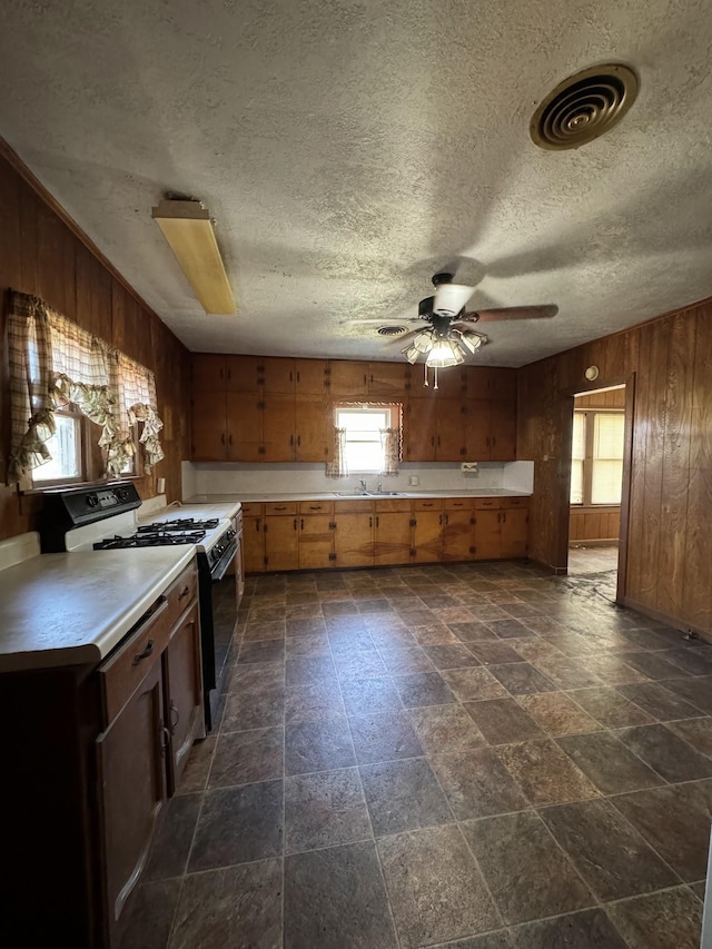 kitchen featuring wood walls, white gas stove, ceiling fan, and sink