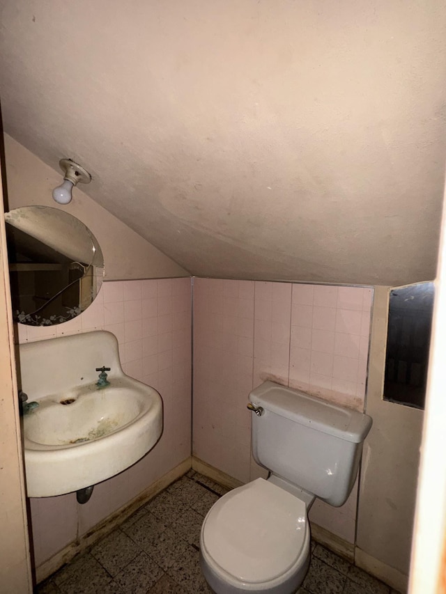 bathroom with tile walls, sink, vaulted ceiling, and toilet