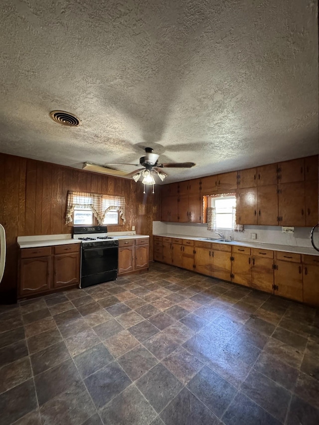 kitchen featuring white range with gas cooktop, wood walls, and ceiling fan