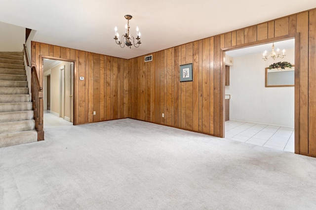 empty room featuring visible vents, wood walls, a chandelier, and light carpet