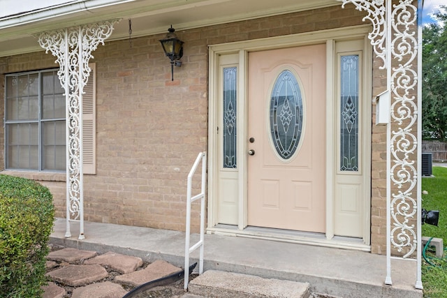 property entrance featuring a porch, central air condition unit, and brick siding