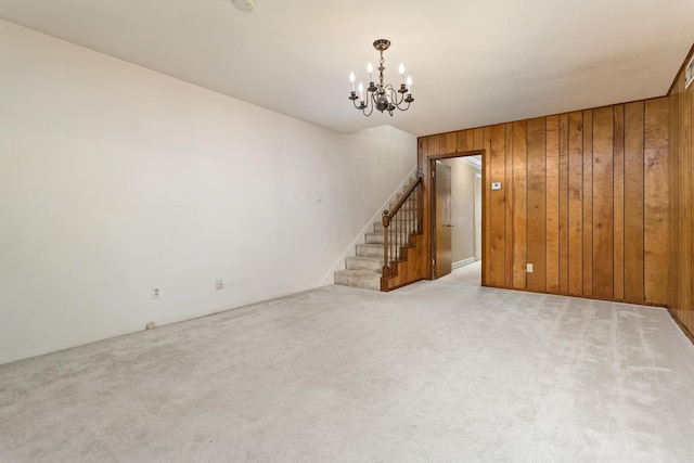 unfurnished living room with an inviting chandelier, stairway, wooden walls, and light carpet