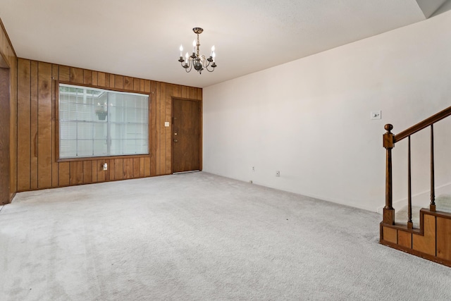 empty room featuring wooden walls, a chandelier, stairs, and carpet