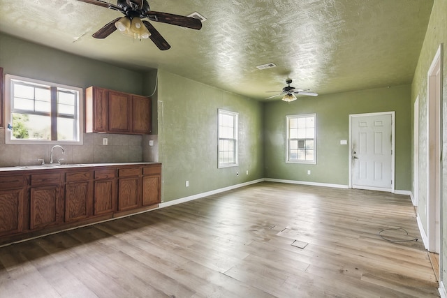 kitchen with a sink, brown cabinets, light wood-type flooring, ceiling fan, and visible vents