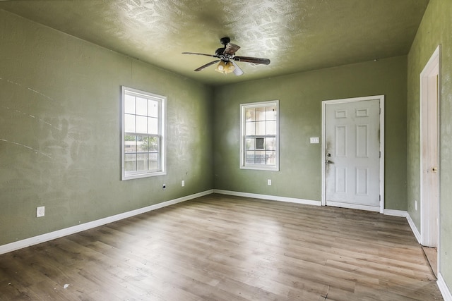 unfurnished room featuring wood finished floors, a wealth of natural light, baseboards, and ceiling fan