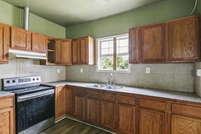 kitchen with a sink, dark wood finished floors, stainless steel range with electric stovetop, brown cabinetry, and under cabinet range hood