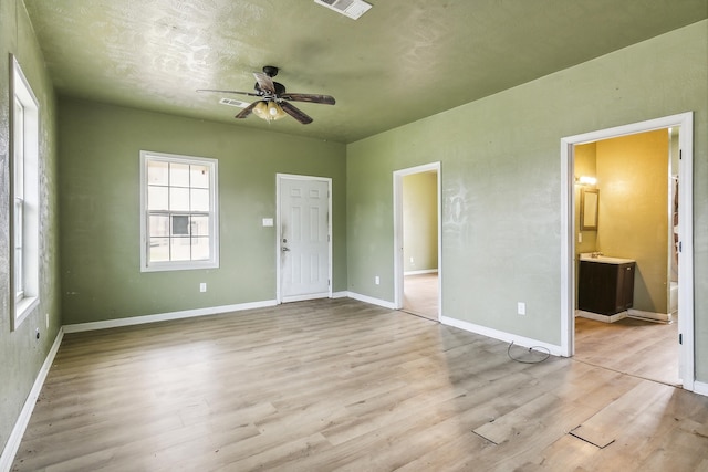 interior space featuring light wood-type flooring, baseboards, ensuite bath, and visible vents