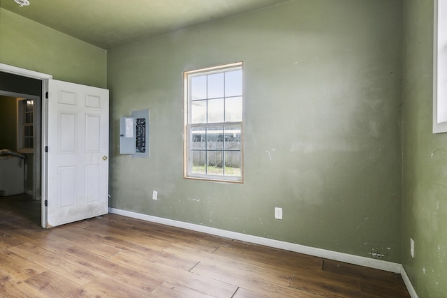 empty room with hardwood / wood-style floors, electric panel, and baseboards