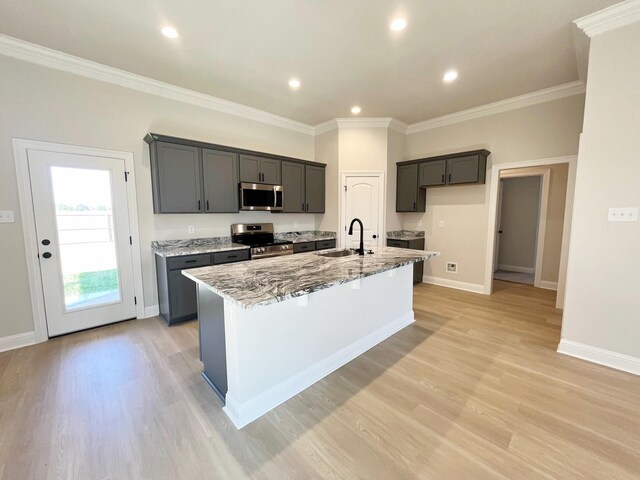 kitchen featuring an island with sink, ornamental molding, a sink, light stone counters, and stainless steel appliances