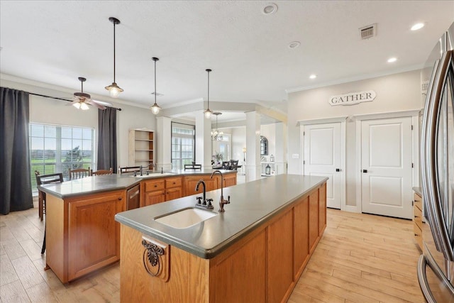 kitchen featuring sink, hanging light fixtures, a kitchen island with sink, crown molding, and light wood-type flooring