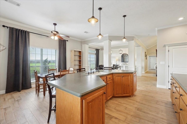 kitchen featuring sink, a kitchen island with sink, a kitchen bar, decorative light fixtures, and light wood-type flooring