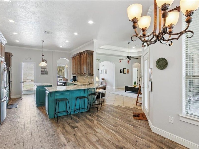 kitchen with ceiling fan with notable chandelier, sink, kitchen peninsula, crown molding, and wood-type flooring