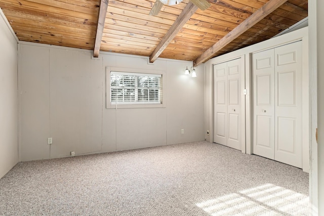 unfurnished bedroom with carpet flooring, vaulted ceiling with beams, wood ceiling, and two closets