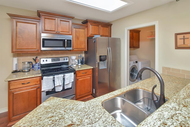 kitchen featuring light stone countertops, tasteful backsplash, stainless steel appliances, sink, and independent washer and dryer