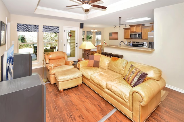 living room featuring a tray ceiling, crown molding, dark hardwood / wood-style flooring, and ceiling fan with notable chandelier