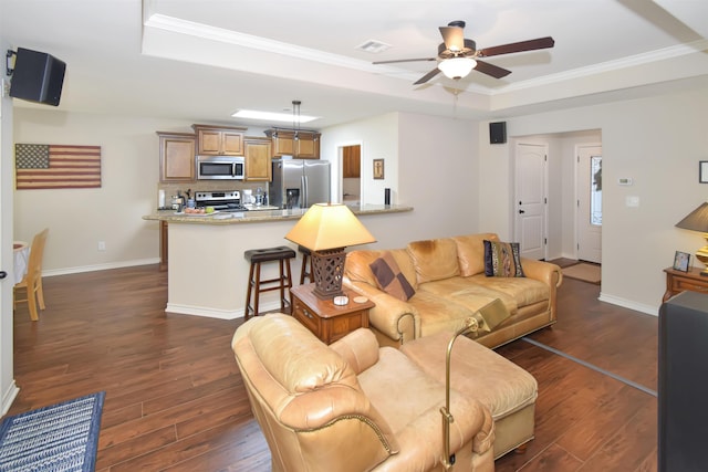 living room with dark hardwood / wood-style floors, ceiling fan, ornamental molding, and a tray ceiling