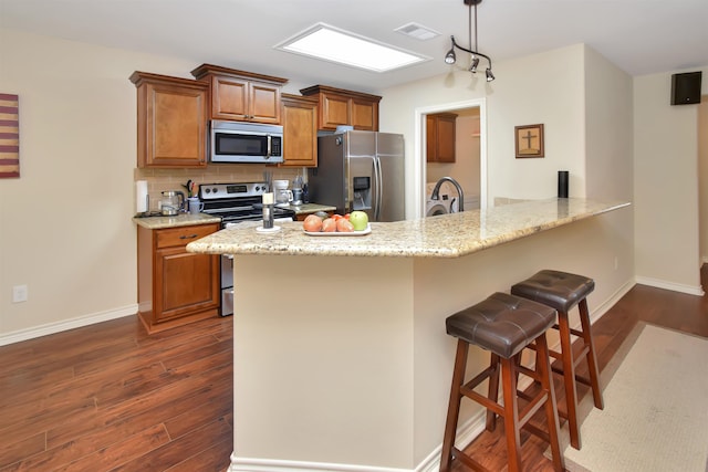 kitchen featuring appliances with stainless steel finishes, backsplash, dark hardwood / wood-style flooring, a kitchen breakfast bar, and decorative light fixtures