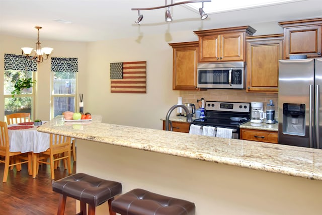 kitchen with light stone counters, pendant lighting, a chandelier, decorative backsplash, and appliances with stainless steel finishes