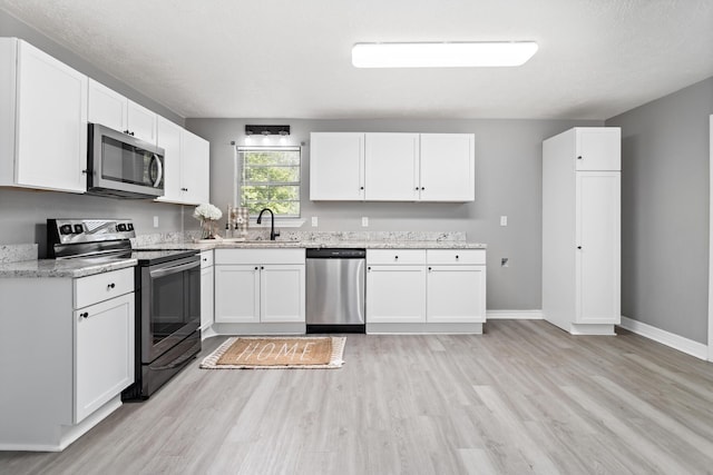 590 Parks St, Silsbee, TX 77656 - kitchen with a sink, white cabinets, light wood-type flooring, light stone countertops, and appliances with stainless steel finishes