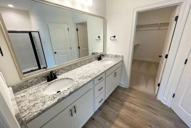 1585 Little Cypress Loop, Orange, TX 77632 - bathroom featuring double vanity, a walk in closet, wood finished floors, a shower stall, and recessed lighting