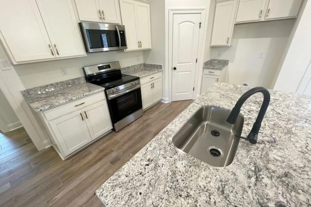1585 Little Cypress Loop, Orange, TX 77632 - kitchen with appliances with stainless steel finishes, wood finished floors, light stone counters, and white cabinets