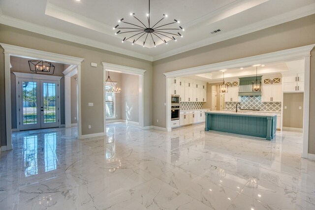 kitchen with a tray ceiling, french doors, a sink, appliances with stainless steel finishes, and an inviting chandelier