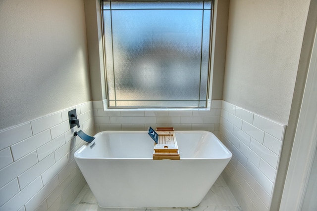 bathroom featuring a soaking tub, a wainscoted wall, tile walls, and marble finish floor