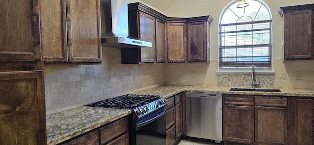 kitchen with black gas range, dishwasher, wall chimney exhaust hood, sink, and light stone counters