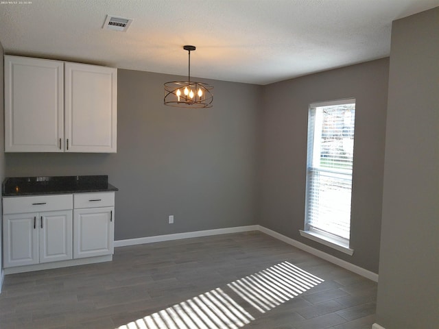 unfurnished dining area featuring dark hardwood / wood-style flooring, a notable chandelier, and a textured ceiling