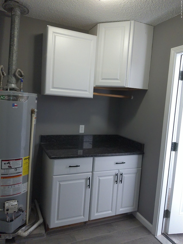 kitchen with wood-type flooring, a textured ceiling, water heater, and white cabinets