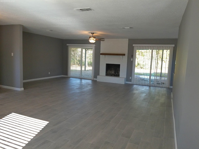 unfurnished living room with hardwood / wood-style flooring, ceiling fan, a fireplace, and a textured ceiling