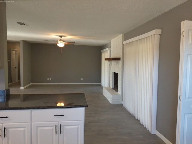 kitchen featuring white cabinetry, dark hardwood / wood-style flooring, ceiling fan, and a fireplace