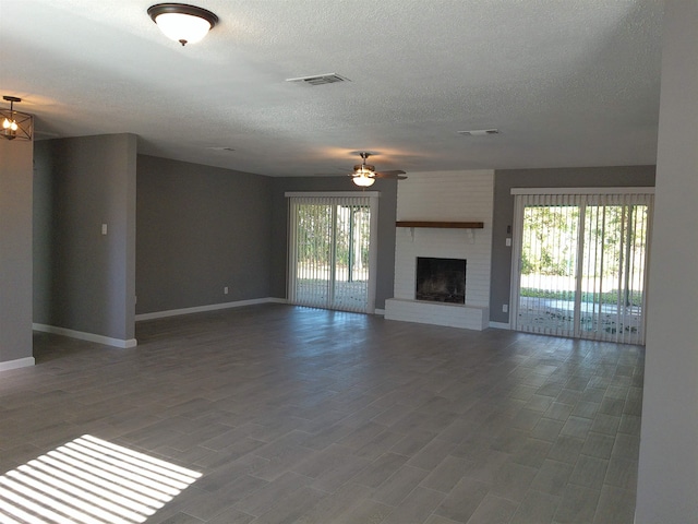 unfurnished living room with ceiling fan with notable chandelier, hardwood / wood-style floors, a brick fireplace, and a textured ceiling