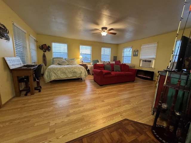 bedroom with cooling unit, ceiling fan, a fireplace, and light wood-type flooring