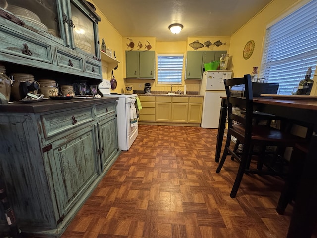 kitchen with dark parquet flooring, sink, green cabinets, and white appliances