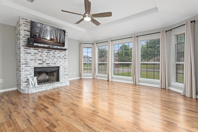 7669 Boardwalk, Lumberton, TX 77657 - unfurnished living room featuring a tray ceiling, ceiling fan, wood finished floors, a brick fireplace, and baseboards