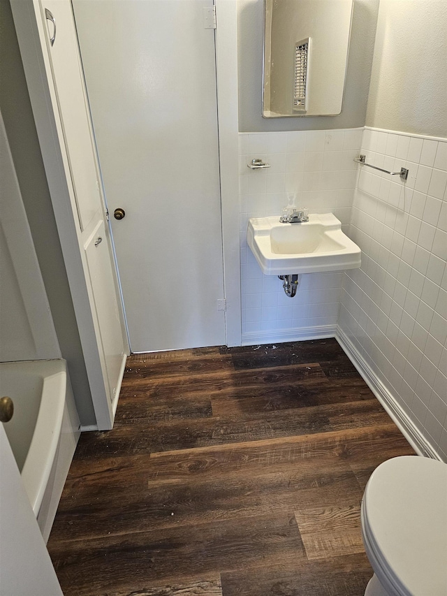 bathroom featuring a tub, sink, toilet, tile walls, and hardwood / wood-style flooring