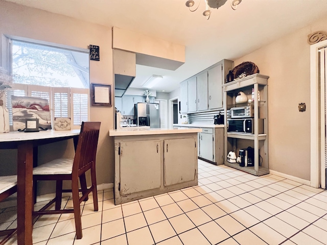 kitchen with gray cabinets, light tile patterned floors, kitchen peninsula, and stainless steel fridge