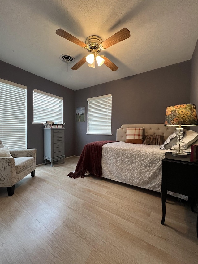 bedroom with a textured ceiling, ceiling fan, and light wood-type flooring