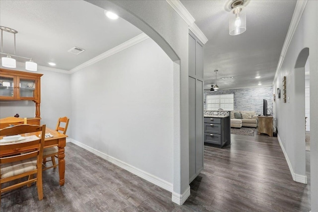 dining area featuring dark wood finished floors, crown molding, baseboards, and arched walkways