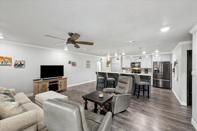 living area with ornamental molding, a textured ceiling, dark wood finished floors, baseboards, and ceiling fan