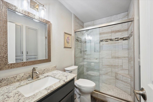 full bathroom with vanity, toilet, a textured wall, and a stall shower