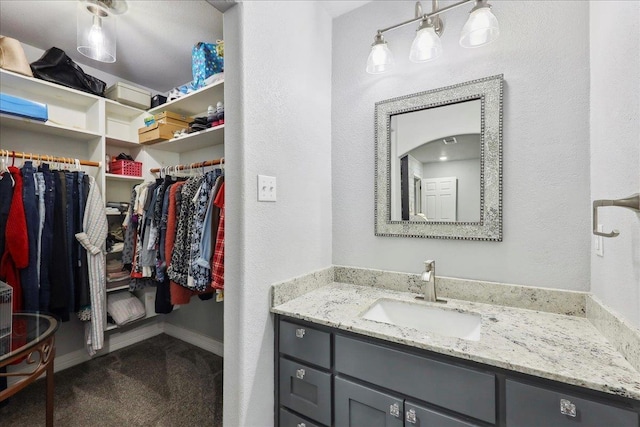 bathroom featuring vanity, a walk in closet, a textured wall, and baseboards