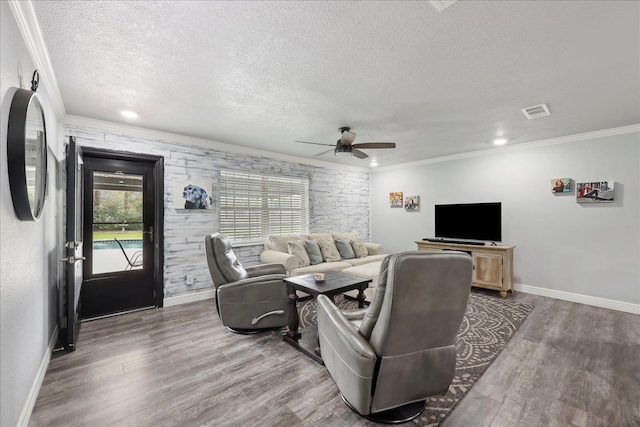 living room with a textured ceiling, wood finished floors, visible vents, and ornamental molding