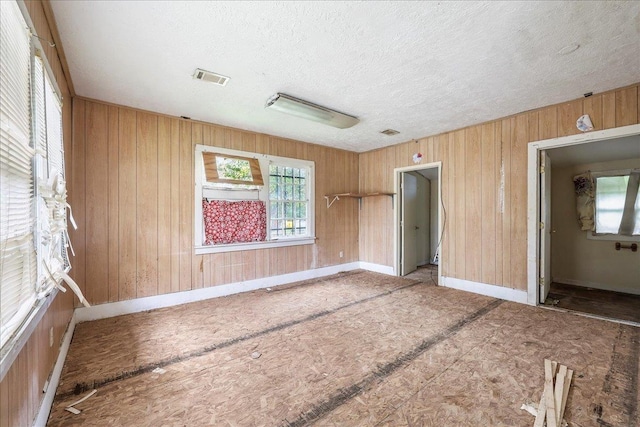 unfurnished room featuring visible vents, a textured ceiling, baseboards, and wooden walls