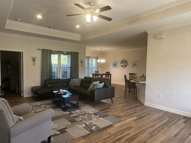 living room with hardwood / wood-style floors, ceiling fan with notable chandelier, a raised ceiling, and ornamental molding