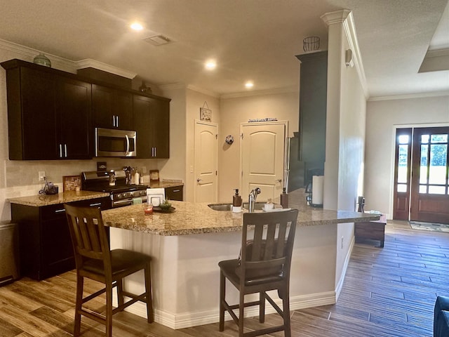 kitchen with a breakfast bar, sink, light wood-type flooring, kitchen peninsula, and stainless steel appliances